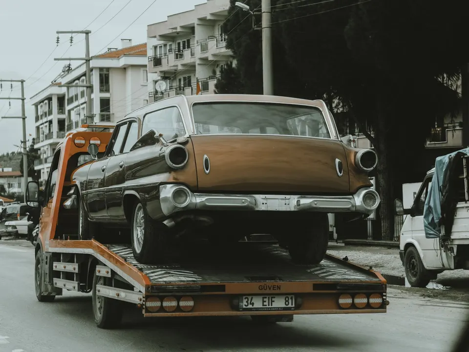 A vintage car being carried by a tow truck on the road