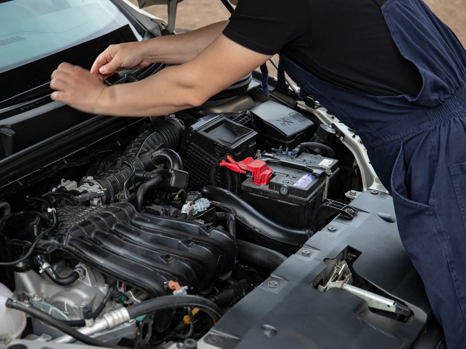 A mechanic working on a car engine outdoors in daylight