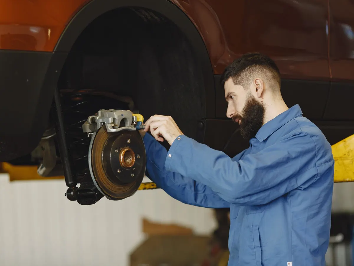 A mechanic in a blue uniform working on a car brake system
