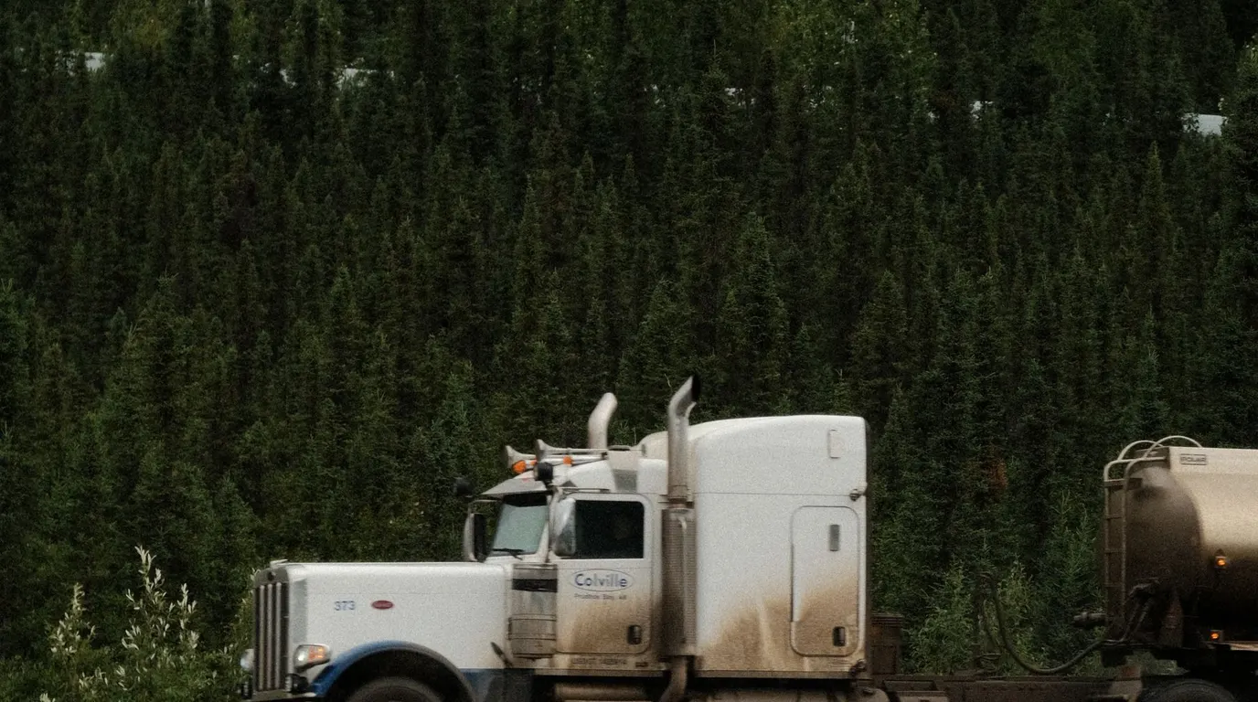 A semi truck parked on a dirt lot by a treeline