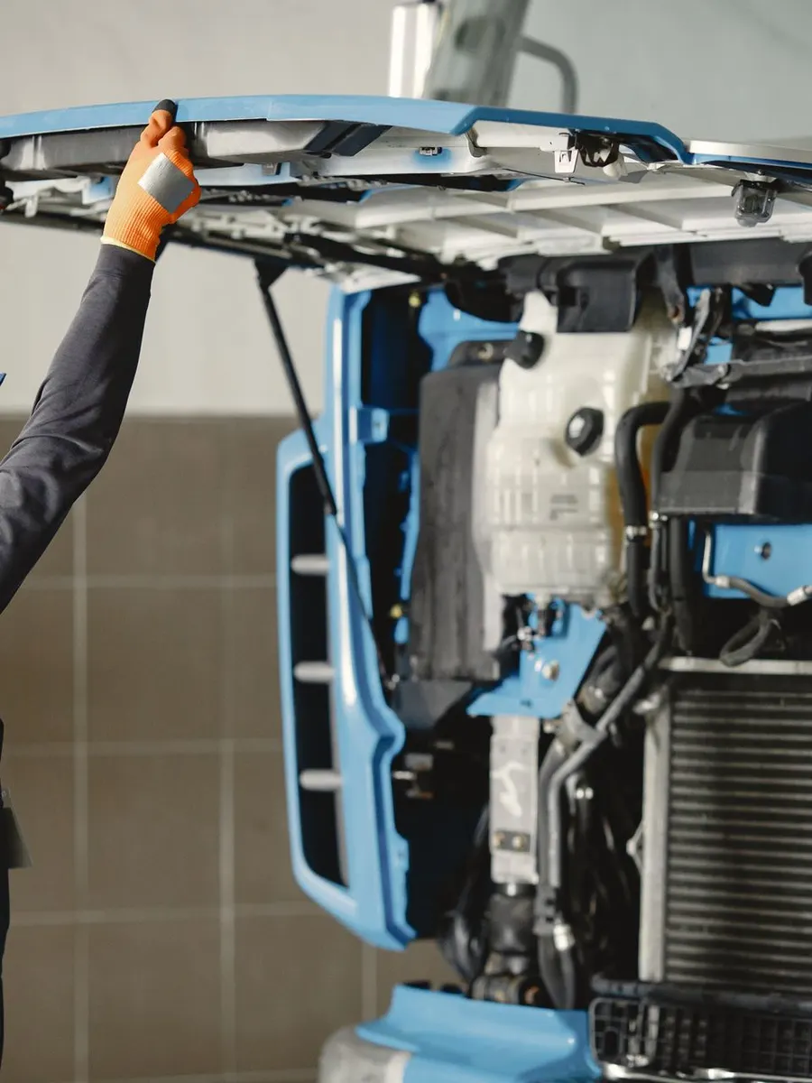 A mechanic looking under the hood of a blue truck
